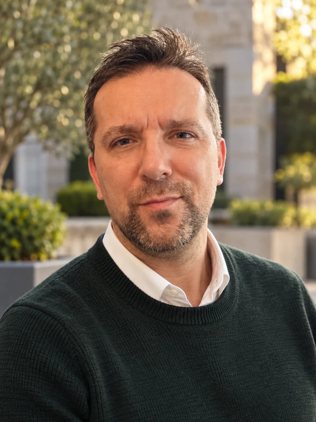 Portrait of Aleksander Celewicz outdoors, wearing a dark green jumper over a white shirt.